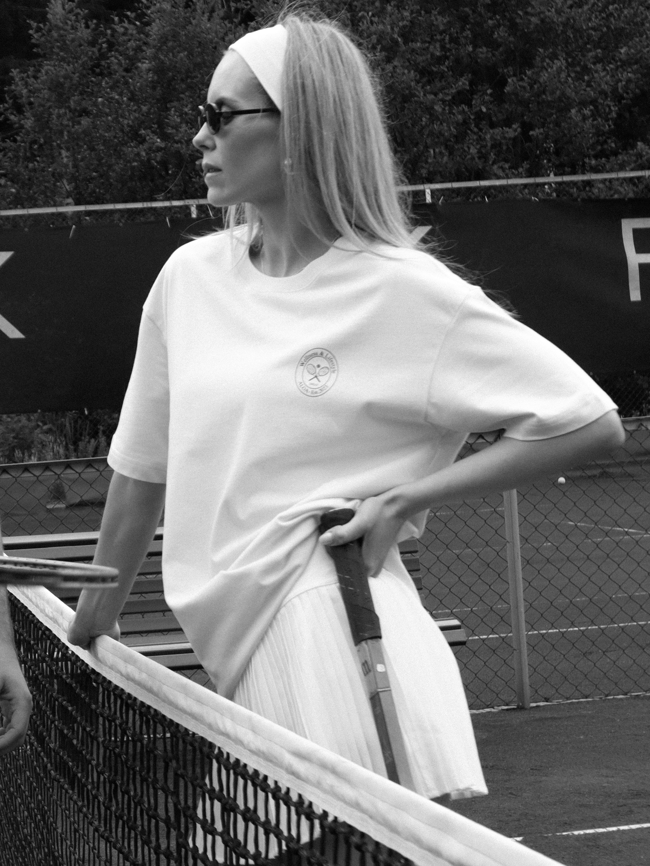 Person on a tennis court wearing a white outfit with a logo